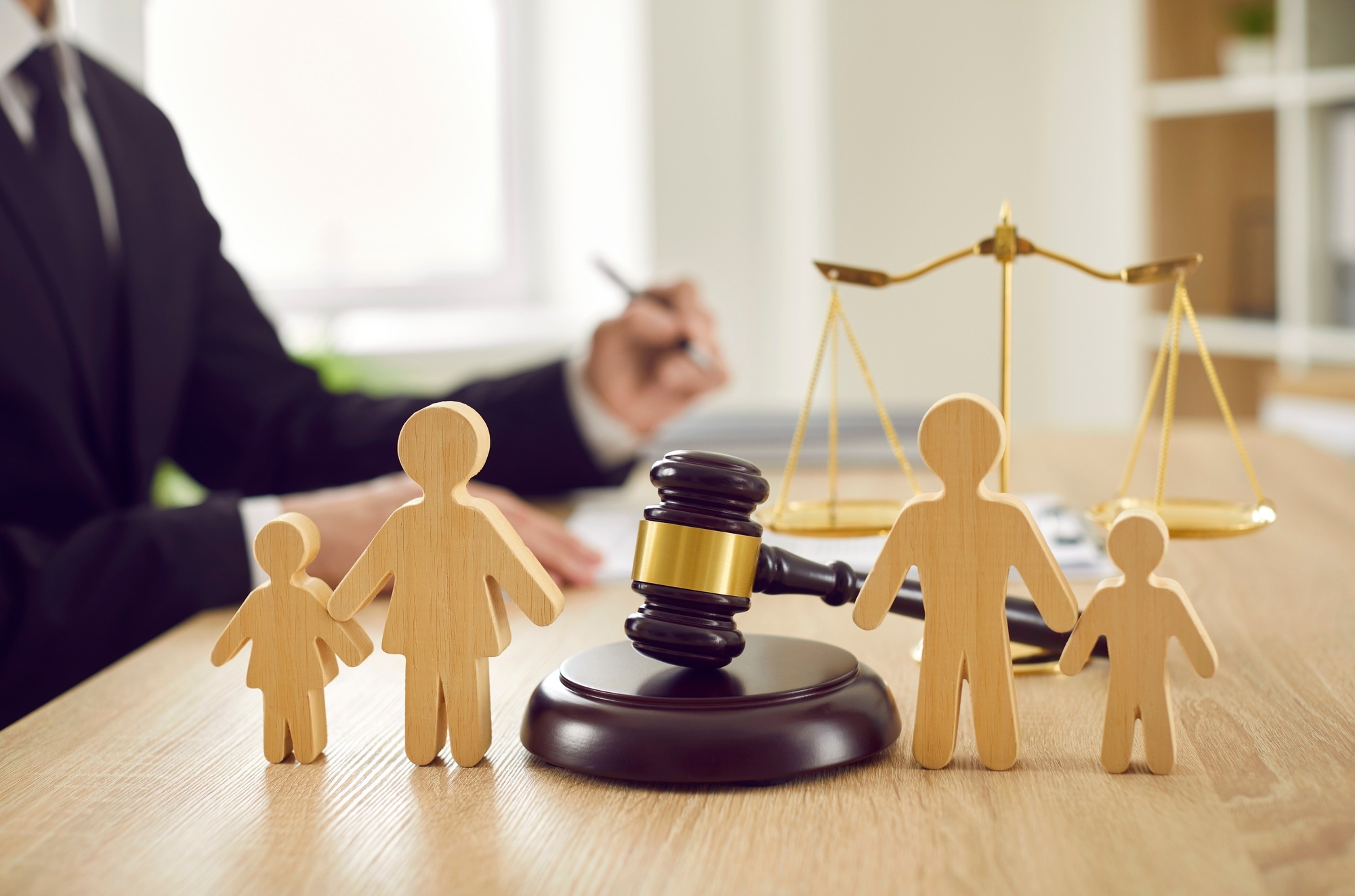Gavel, Sound Block and Little Wooden Figures of Parents and Children Placed on Desk in Courthouse up Close, Judge and Scales of Justice in Background. Family Law, Court, Divorce, Child Custody Concept.