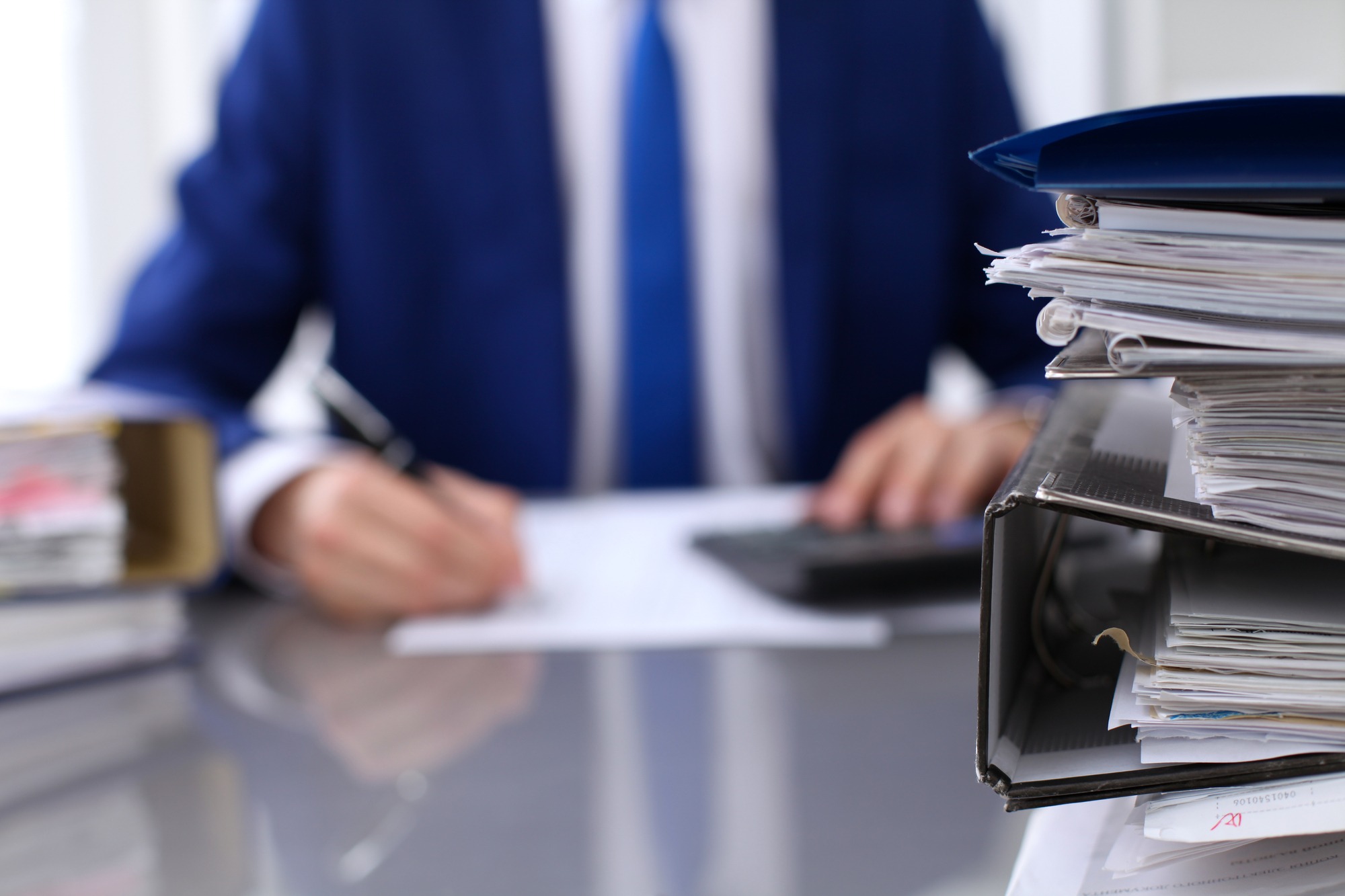 Binders With Papers Are Waiting to Be Processed With Businessman Back in Blur. Accounting Planning Budget, Audit, Insurance And Business Concept